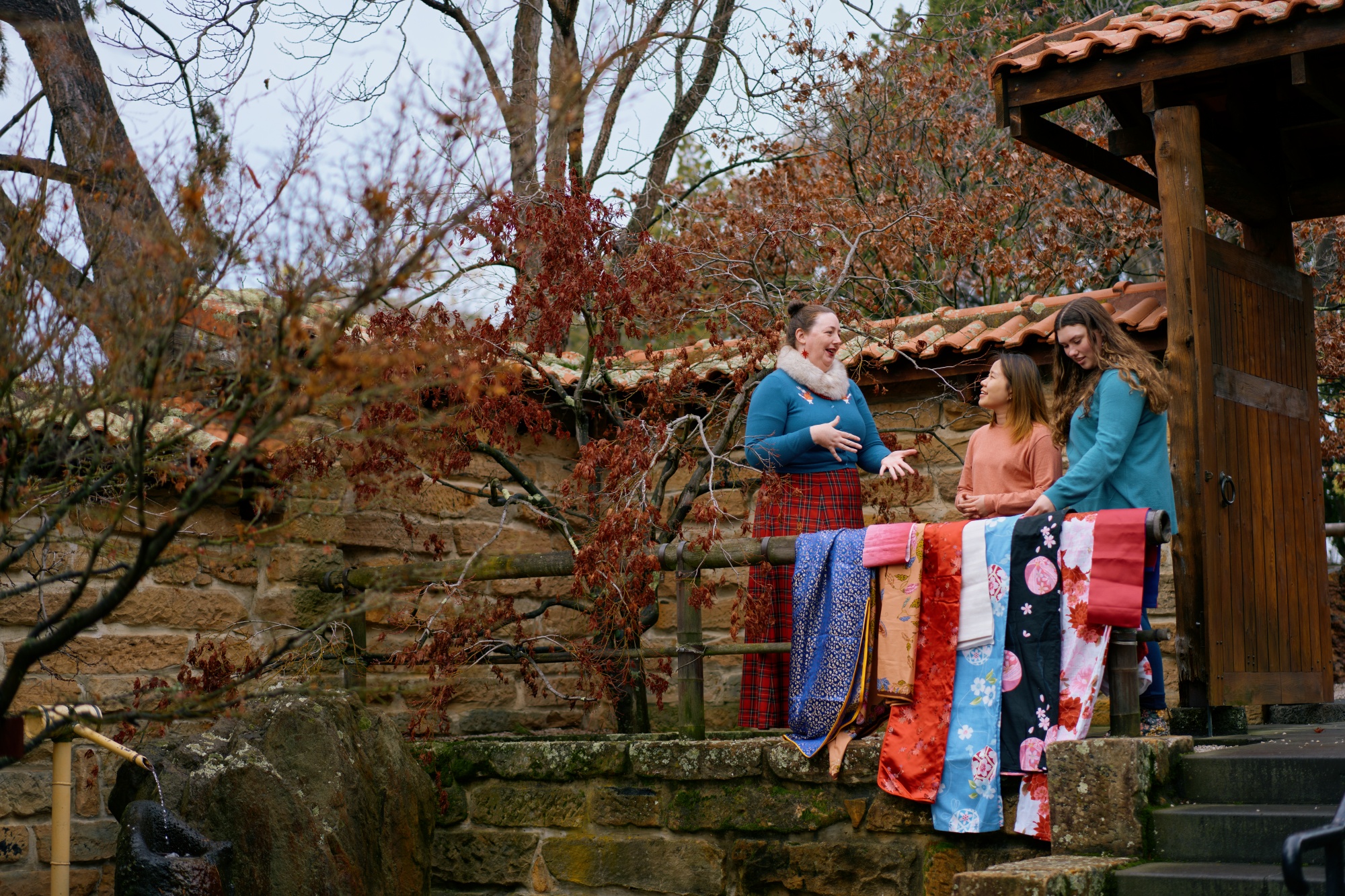 Lecturer with male and female student in Japanese garden with traditional silks laid over a ledge