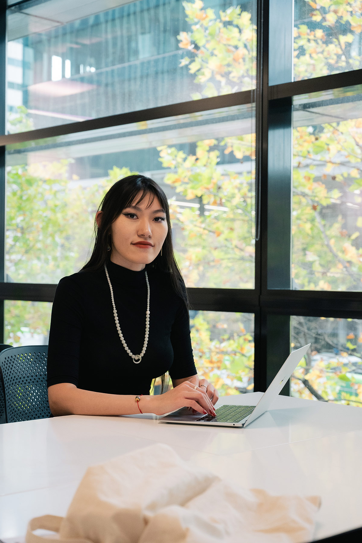 Tianyi seated at a desk using a laptop in a study space, with large windows and leafy trees visible outside.