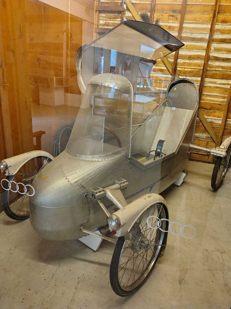Vintage electric vehicle with a metallic body and transparent canopy, displayed indoors
